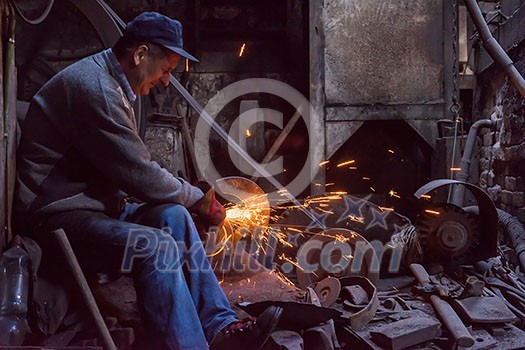 the blacksmith polishing metal products making sparks while using a grinding machine in his traditional workshop the blacksmith polishing metal products making sparks while using a grinding machine in his traditional workshop