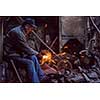 the blacksmith polishing metal products making sparks while using a grinding machine in his traditional workshop