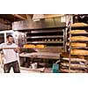 bakery worker taking out freshly baked breads with shovel from the professional oven at the manufacturing