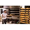 bakery worker taking out freshly baked breads with shovel from the professional oven at the manufacturing