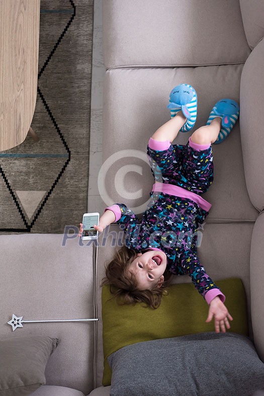 top view of cute little girl using a smartphone and smiling while lying on the sofa at home top view of cute little girl using a smartphone and smiling while lying on the sofa at home