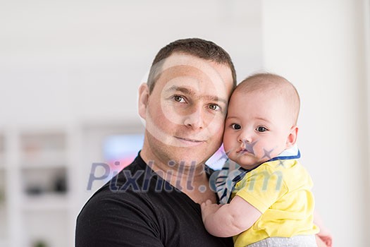 portrait of happy young father holding newborn baby boy near the window at home