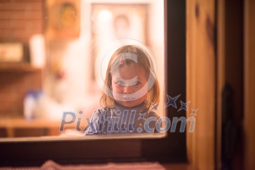 outside view of happy little cute girl playing near the window during winter time at home