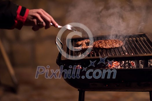 young man cooking meat on barbecue in front of the weekend house on a cold winter day young man cooking meat on barbecue in front of the weekend house on a cold winter day