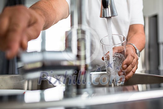 Hands of a senior man pouring a glass of water in a modern kitchen