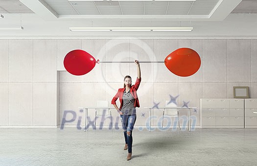 Young woman in modern interior lifting balloon barbell above head