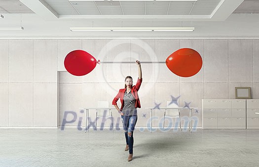 Young woman in modern interior lifting balloon barbell above head Young woman in modern interior lifting balloon barbell above head