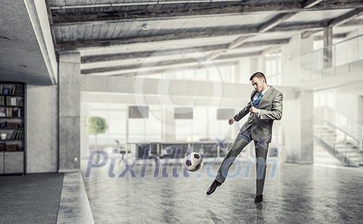 Businessman in suit in modern office jumping to hit soccer ball