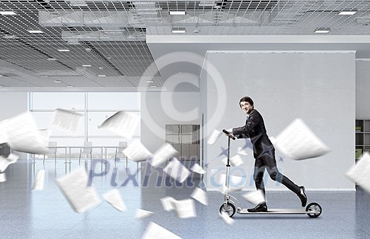 Young cheerful businessman in suit riding scooter in office Young cheerful businessman in suit riding scooter in office