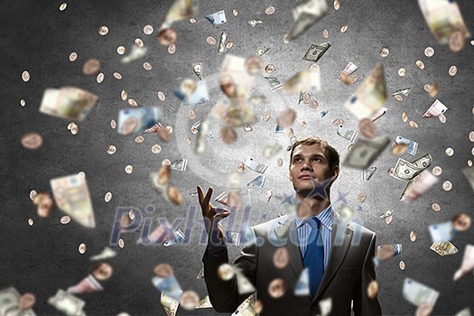 Young businessman standing in the rain of money banknotes