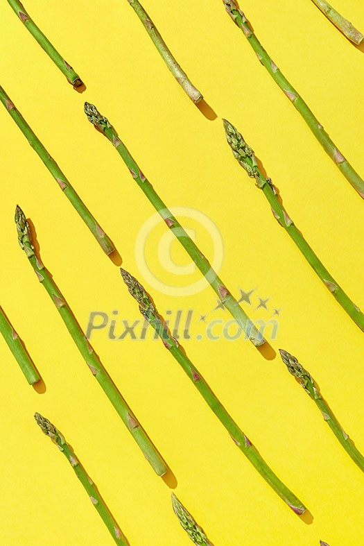 Diagonal pattern of freshly picked natural green asparagus on an yellow background with shadows. Top view. Vegetarian nutrition concept.