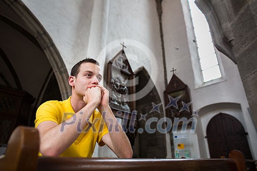 Handsome young man praying in a church Handsome young man praying in a church