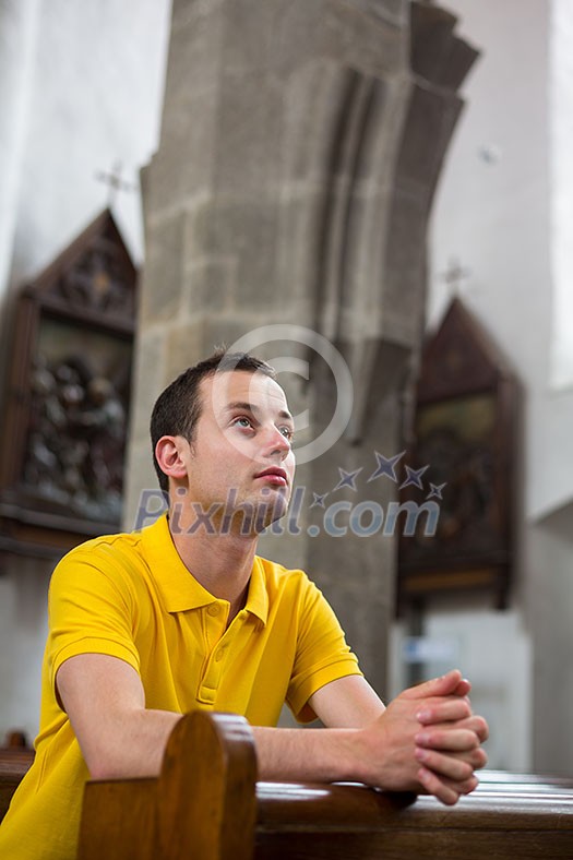 Handsome young man praying in a church Handsome young man praying in a church