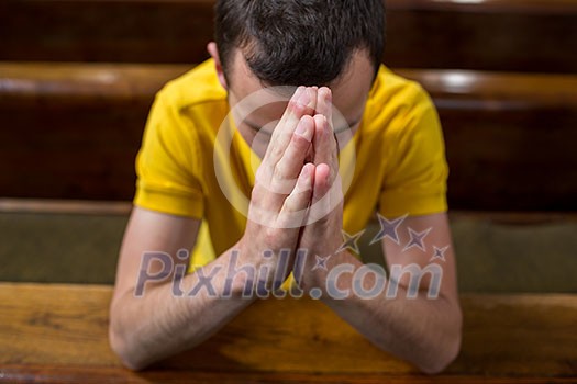 Handsome young man praying in a church Handsome young man praying in a church