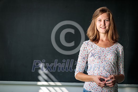 Pretty, young female student/young teacxher in front of a blackboard during class