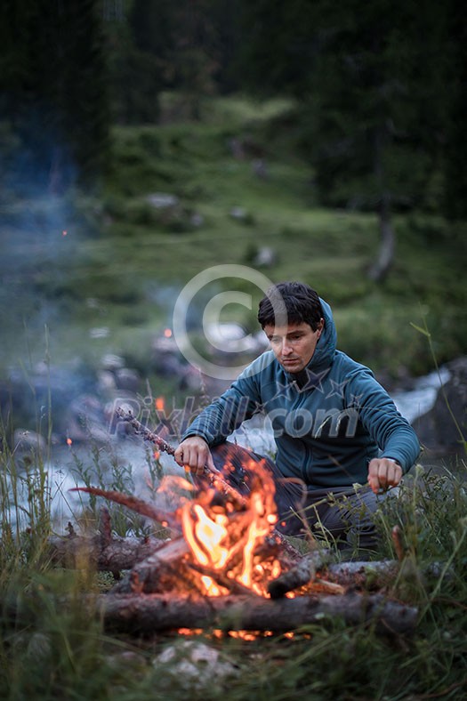 Young man making fire while camping outdoors, in an alpine wilderness