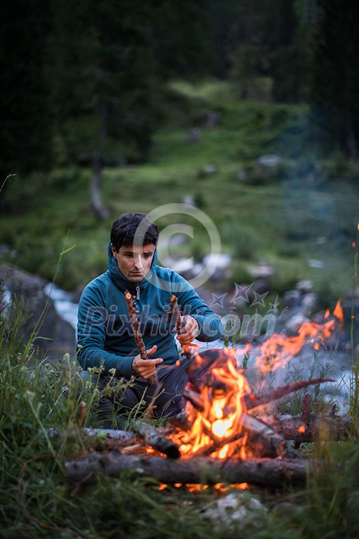 Young man making fire while camping outdoors, in an alpine wilderness