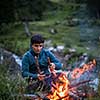 Young man making fire while camping outdoors, in an alpine wilderness