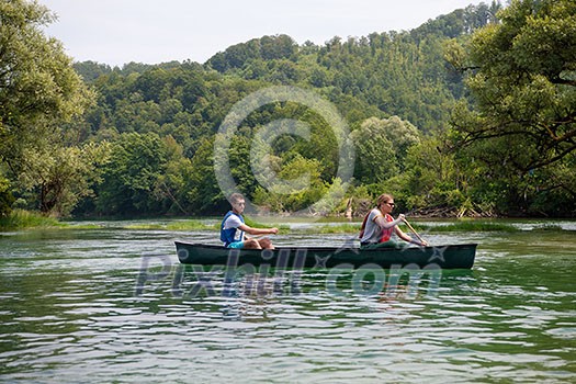 Couple adventurous explorer friends are canoeing in a wild river surrounded by the  beautiful nature