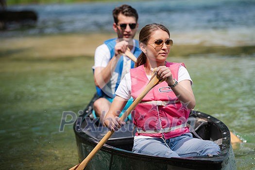 Couple friends are canoeing in a wild river surrounded by the  beautiful nature