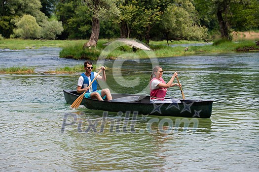 Couple friends are canoeing in a wild river surrounded by the  beautiful nature