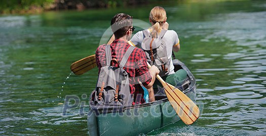 Couple adventurous explorer friends are canoeing in a wild river surrounded by the  beautiful nature