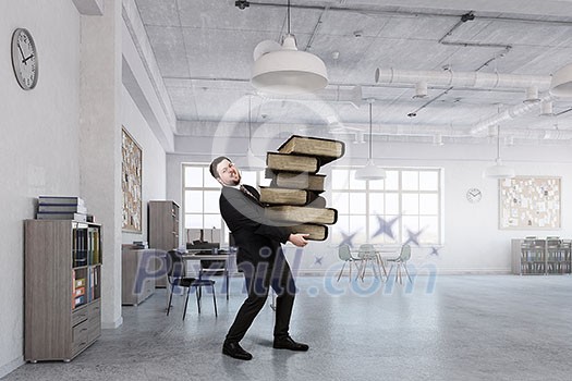 Young businessman in modern office carrying pile of books