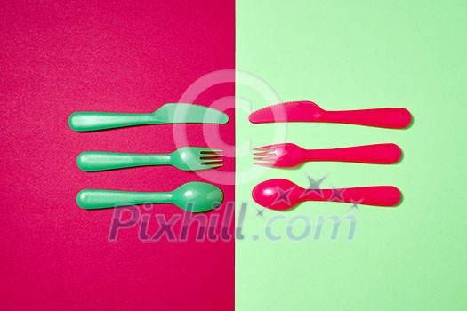 Multicolored set of plastic tableware on a duotone background with copy space. Top view. Multicolored set of plastic tableware on a duotone background with copy space. Top view.