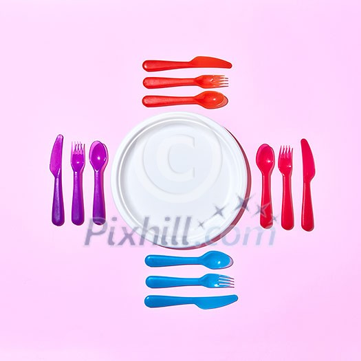 Eating set from disposable plastic cutlery, serving around paper white plate on a pastel pink background with copy space. Flat lay. Eating set from disposable plastic cutlery, serving around paper white plate on a pastel pink background with copy space. Flat lay.