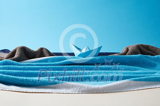 Handcraft sea waves and stone rocks made from fluffy towels and blue ship on a paper background with copy space.