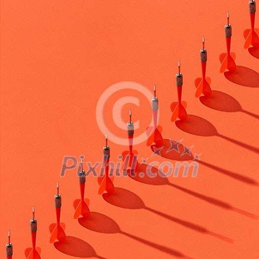 Vertical darts in a diagonal line with shadows on an orange background, copy space.