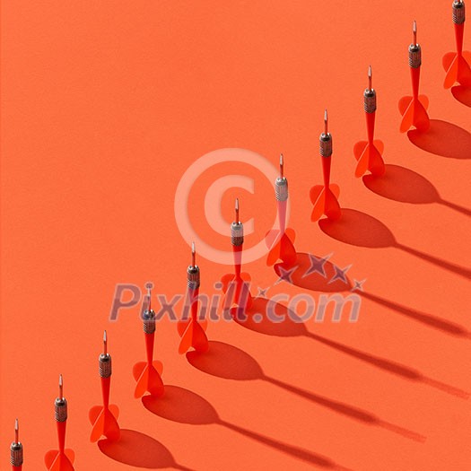 Vertical darts in a diagonal line with shadows on an orange background, copy space. Vertical darts in a diagonal line with shadows on an orange background, copy space.
