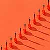 Vertical darts in a diagonal line with shadows on an orange background, copy space.