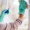 Young Smiling Woman Washing Window with Sponge. Happy Beautiful Girl wearing Protective Gloves Cleaning Window by spraying Cleaning Products and wiping with Sponge. Woman Cleaning House
