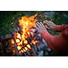 Young woman making fire while camping outdoors, in an alpine wilderness - warming up her hands near the fire