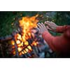 Young woman making fire while camping outdoors, in an alpine wilderness - warming up her hands near the fire