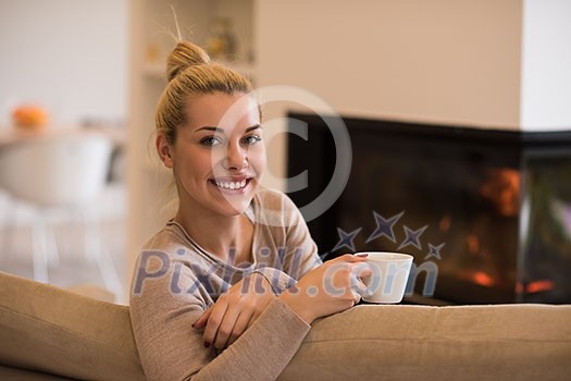 Portrait of beautiful young woman with a mug near a fireplace
