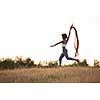 Young beautiful black girl laughs and dances outdoors with a scarf in her hands in a meadow during sunset