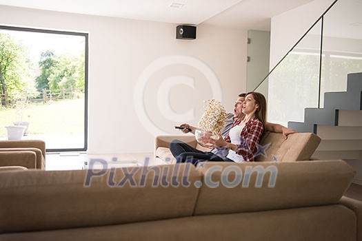 young handsome couple enjoying free time watching television with popcorn in their luxury home villa young handsome couple enjoying free time watching television with popcorn in their luxury home villa