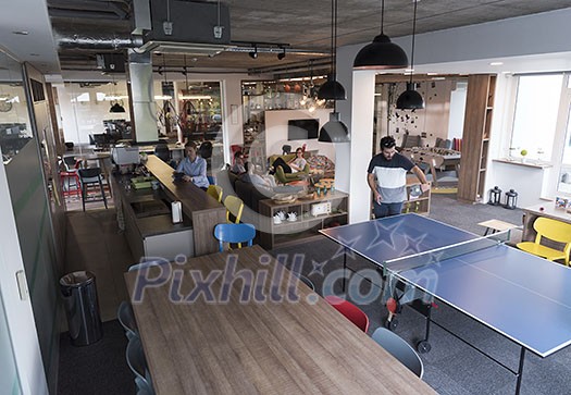 Two young start up business man playing ping pong tennis at modern creative office space people group have meeting and brainstorming in background Two young start up business man playing ping pong tennis at modern creative office space people group have meeting and brainstorming in background