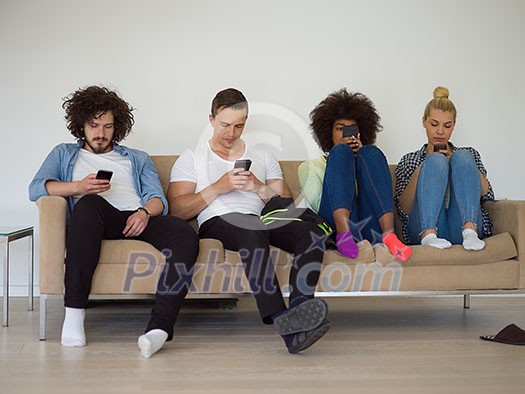 multiethnic group of young people sitting on a sofa at home,staring at smartphone, being antisocial, smartphone addiction