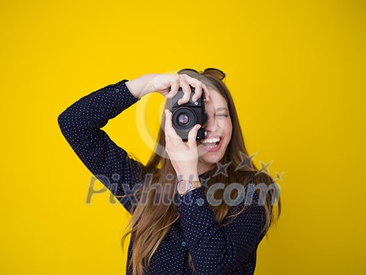 portrait of a smiling pretty girl taking photo on a retro camera isolated over yellow background