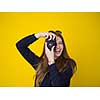 portrait of a smiling pretty girl taking photo on a retro camera isolated over yellow background