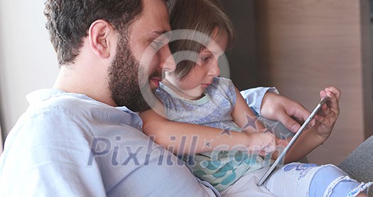 Father Daughter sitting in sofa  playing games on tablet