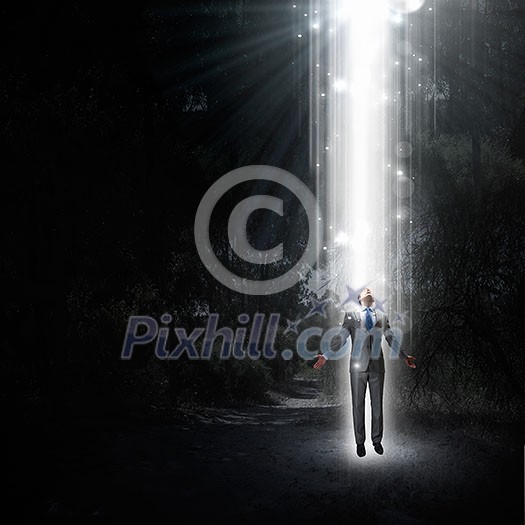 Businessman with hands spread apart standing in light coming from above Businessman with hands spread apart standing in light coming from above