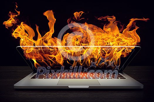 Laptop in fire flames on dark background. Mixed media Laptop in fire flames on dark background. Mixed media