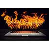 Laptop in fire flames on dark background. Mixed media