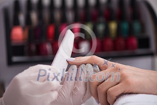 Woman hands receiving a manicure in beauty salon. Nail filing. Close up, selective focus.