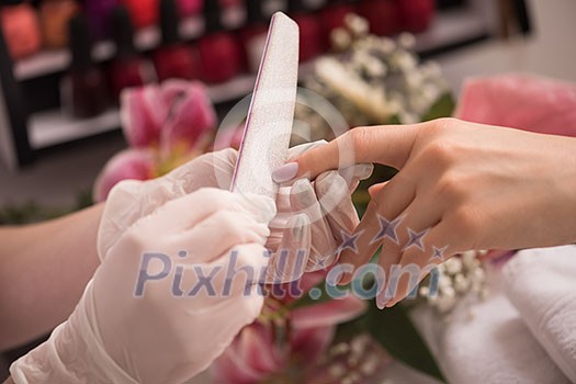 Woman hands receiving a manicure in beauty salon. Nail filing. Close up, selective focus.