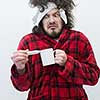 young Man with flu and fever wrapped holding cup of healing tea isolated over white